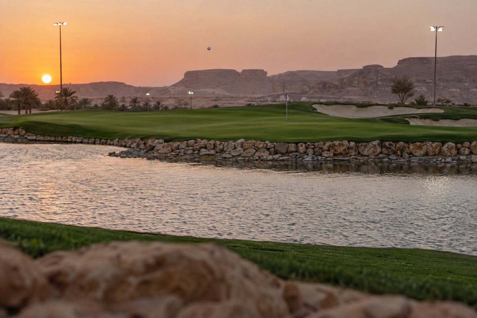 Ball in flight over a water hazard toward a floodlit green